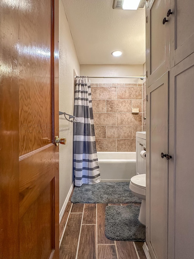 bathroom with shower / tub combo with curtain, toilet, and a textured ceiling