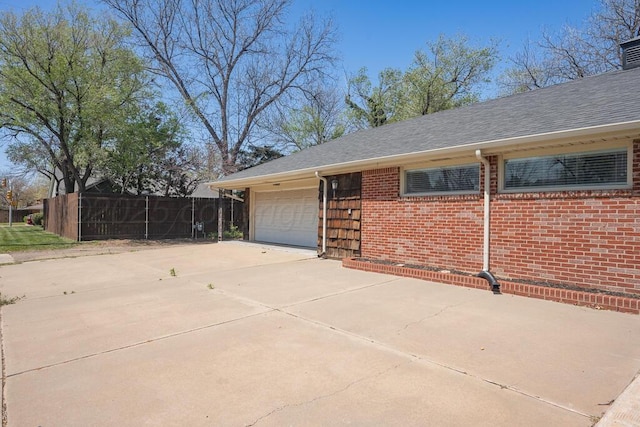 view of side of home with roof with shingles, fence, brick siding, a garage, and concrete driveway