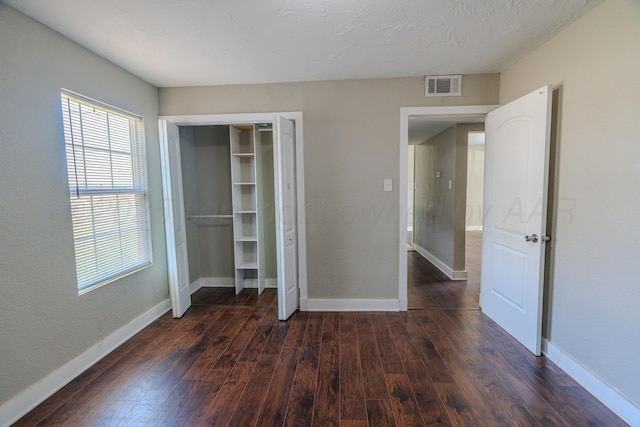 unfurnished bedroom featuring dark wood-style floors, baseboards, and a closet