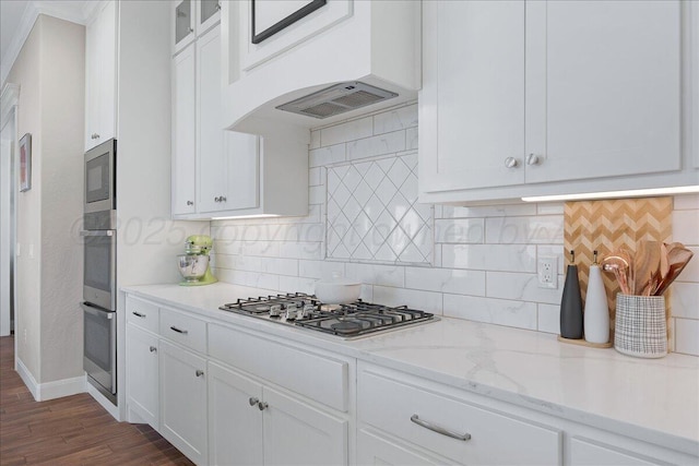 kitchen with stainless steel appliances, white cabinetry, light stone counters, and dark wood finished floors