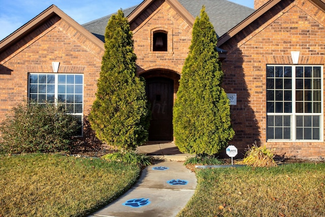 view of front of property featuring brick siding, a front lawn, and a shingled roof