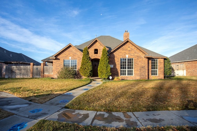 view of front of home with roof with shingles, fence, a front lawn, brick siding, and a chimney