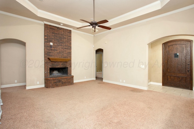 unfurnished living room with arched walkways, a ceiling fan, a fireplace, a tray ceiling, and light colored carpet