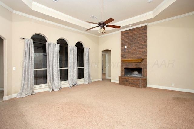 unfurnished living room with a raised ceiling, arched walkways, a brick fireplace, ceiling fan, and carpet floors