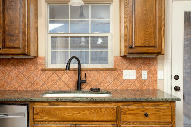 kitchen featuring brown cabinetry, a sink, dark stone counters, and decorative backsplash