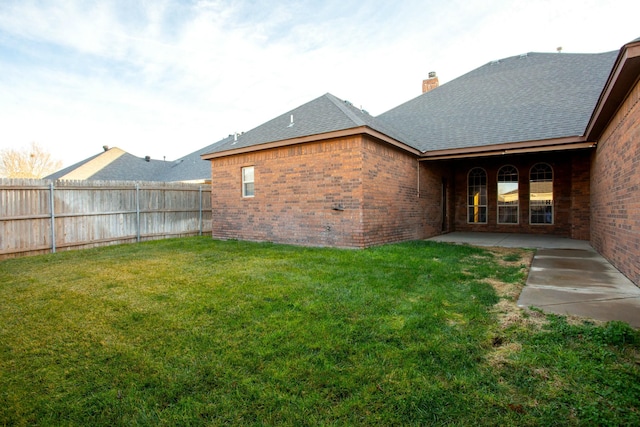 rear view of property featuring a chimney, brick siding, a yard, fence, and a shingled roof