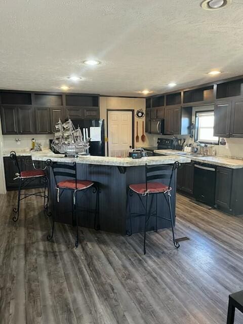 kitchen with dishwasher, a kitchen bar, hardwood / wood-style flooring, a center island, and a textured ceiling