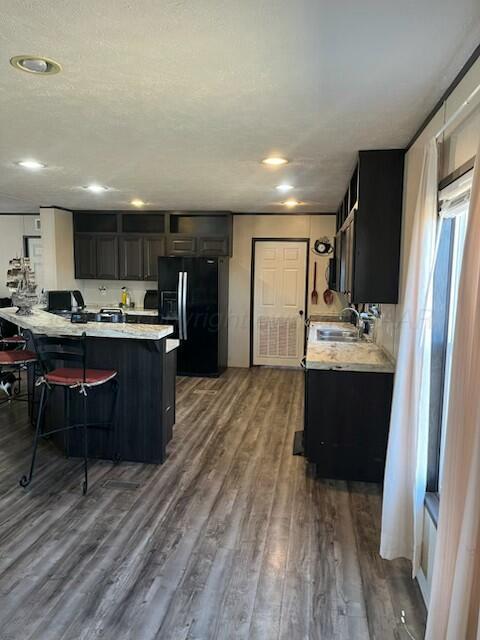 kitchen featuring sink, a breakfast bar area, hardwood / wood-style floors, black refrigerator with ice dispenser, and kitchen peninsula