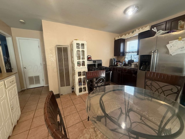 kitchen with stainless steel fridge, gas range oven, dark brown cabinets, and light tile patterned floors