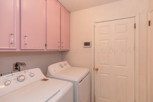 clothes washing area with washer and dryer, a textured ceiling, and cabinet space