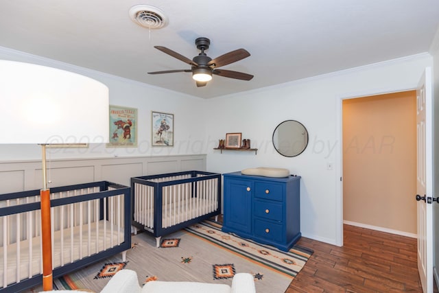 bedroom featuring crown molding, visible vents, a crib, and wood finished floors