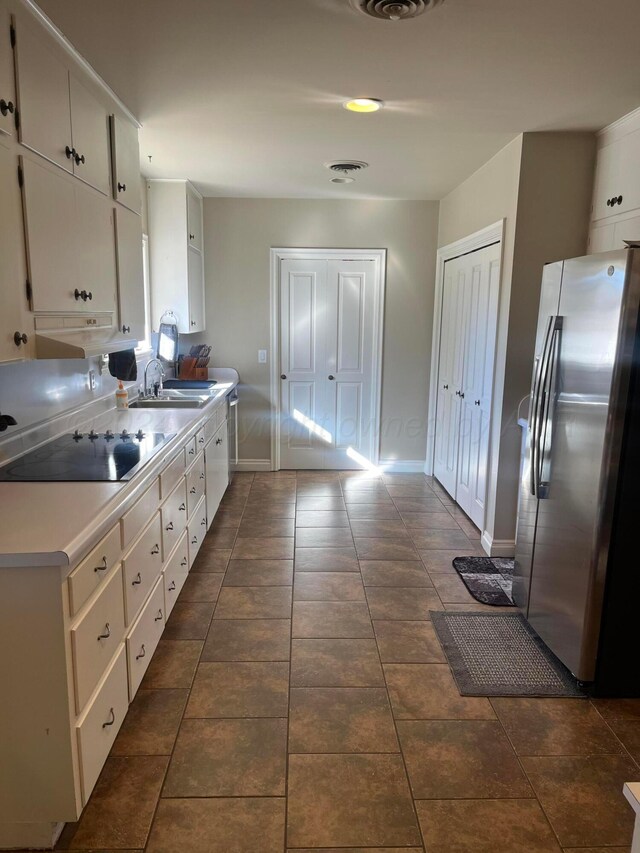 kitchen with white cabinetry, black electric cooktop, a sink, and freestanding refrigerator