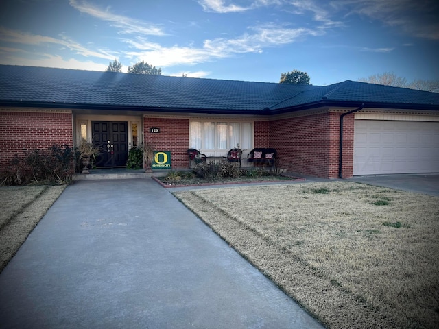 ranch-style home featuring driveway, a tile roof, brick siding, and an attached garage