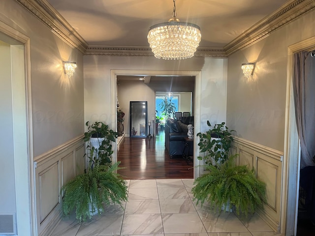 hallway featuring ornamental molding, a chandelier, and wainscoting