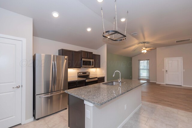 kitchen featuring dark brown cabinetry, appliances with stainless steel finishes, a sink, an island with sink, and a ceiling fan