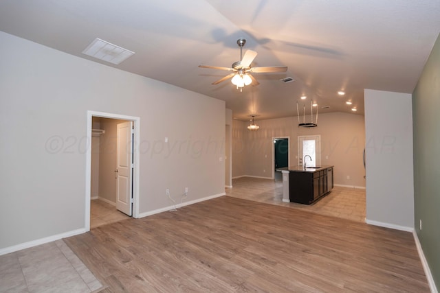 unfurnished living room featuring light wood-style flooring, a ceiling fan, baseboards, vaulted ceiling, and visible vents