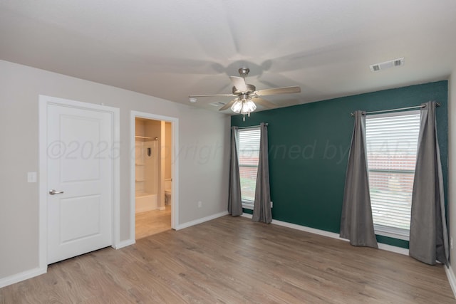 interior space featuring ceiling fan, ensuite bath, baseboards, light wood-type flooring, and visible vents
