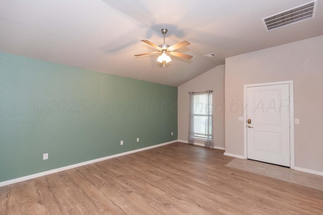 empty room with a ceiling fan, vaulted ceiling, wood finished floors, and visible vents