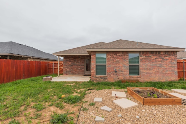 back of house with brick siding, a vegetable garden, a fenced backyard, a patio area, and a yard
