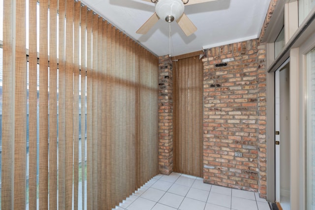 tiled empty room featuring ceiling fan and brick wall