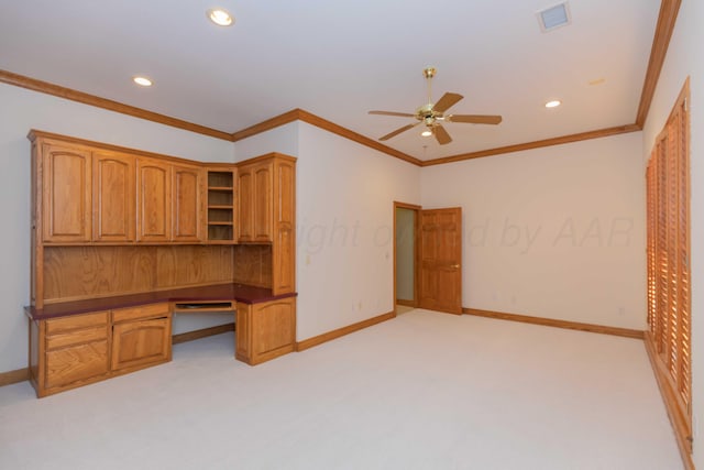 unfurnished office with crown molding, light colored carpet, built in desk, and ceiling fan