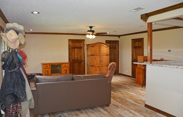 living room featuring light wood-type flooring, a textured ceiling, ceiling fan, and crown molding