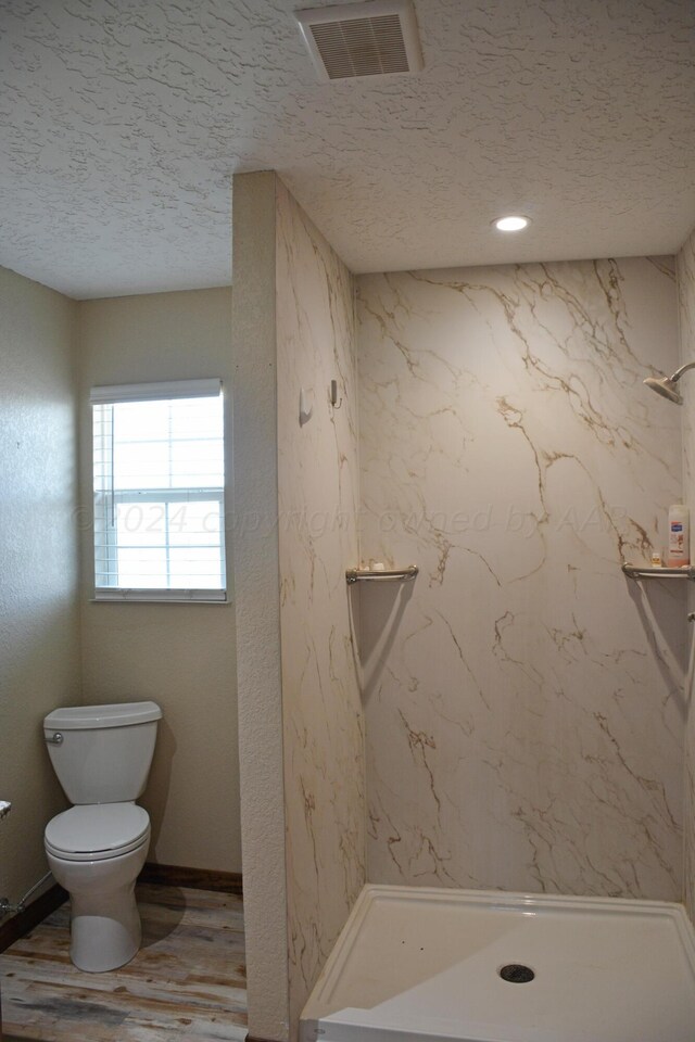 bathroom featuring hardwood / wood-style flooring, a textured ceiling, toilet, and a tile shower