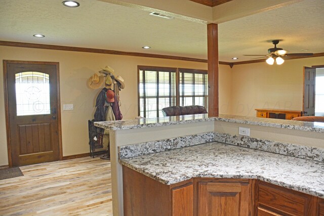 kitchen featuring ornamental molding, ceiling fan, light stone counters, and light hardwood / wood-style floors