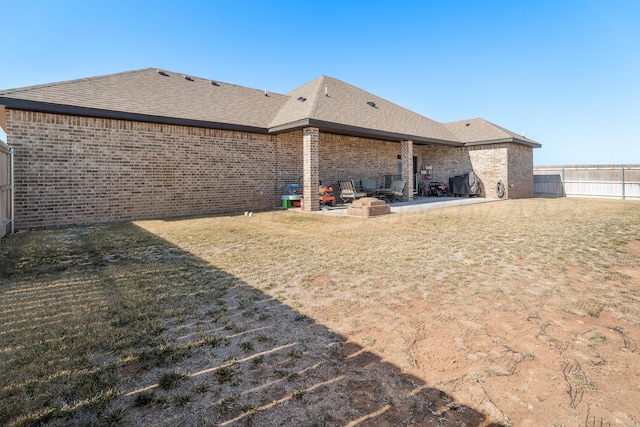 back of property with fence, a yard, roof with shingles, brick siding, and a patio area
