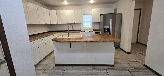 kitchen with a center island with sink, white cabinetry, butcher block counters, and sink