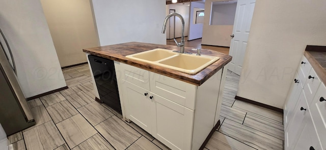 kitchen featuring butcher block countertops, a kitchen island with sink, sink, and white cabinets