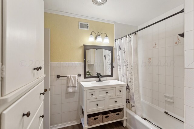 full bathroom with tile walls, vanity, shower / tub combo, visible vents, and ornamental molding