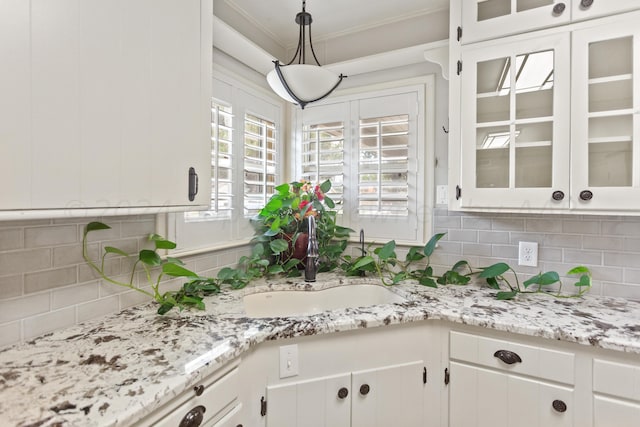 kitchen featuring crown molding, backsplash, a sink, white cabinets, and glass insert cabinets