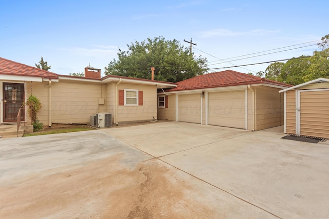 exterior space with an outdoor structure, central air condition unit, a tiled roof, a storage unit, and a chimney