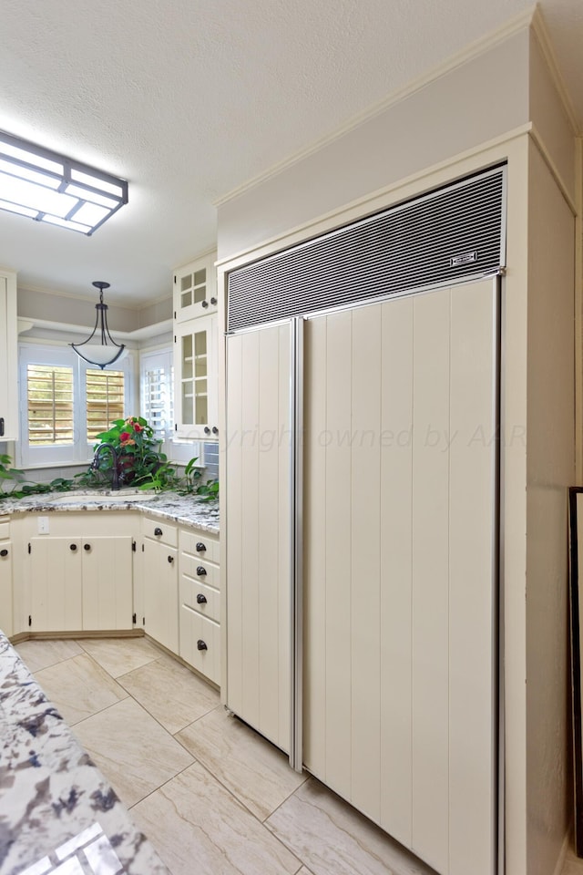 kitchen featuring white cabinetry, a textured ceiling, hanging light fixtures, light stone counters, and glass insert cabinets