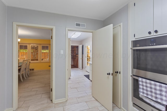 interior space featuring white cabinets, stainless steel double oven, ornamental molding, and visible vents