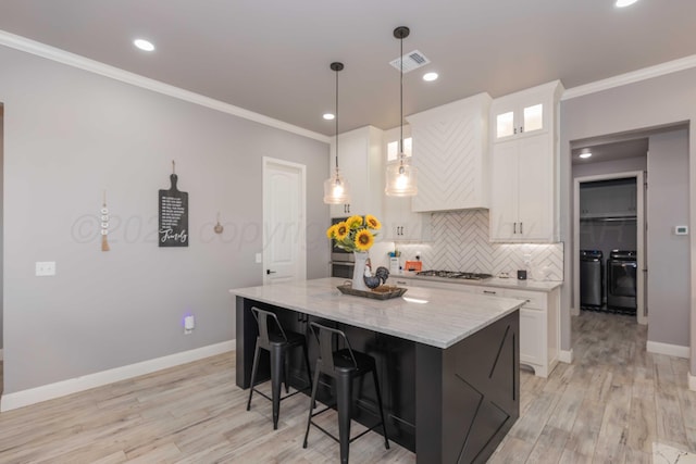 kitchen with a kitchen island, white cabinetry, hanging light fixtures, washer and clothes dryer, and stainless steel gas cooktop