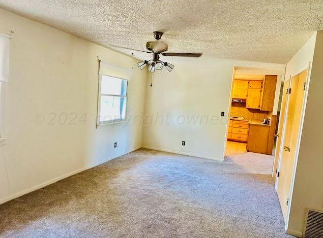 spare room featuring a textured ceiling, light colored carpet, and ceiling fan