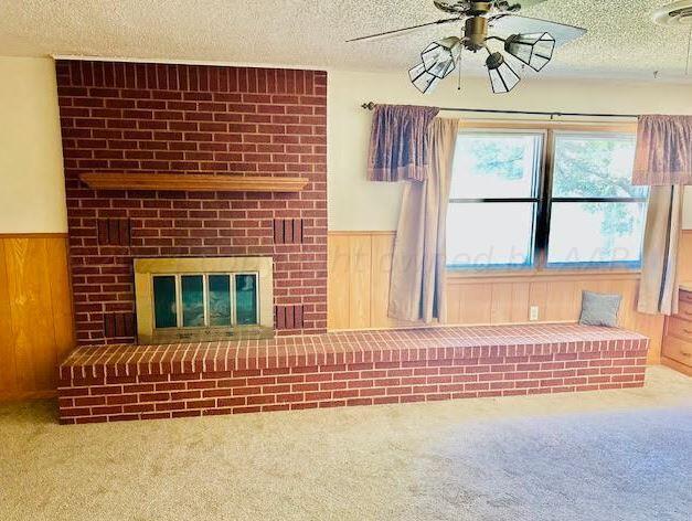 unfurnished living room with wood walls, a textured ceiling, carpet flooring, and a fireplace