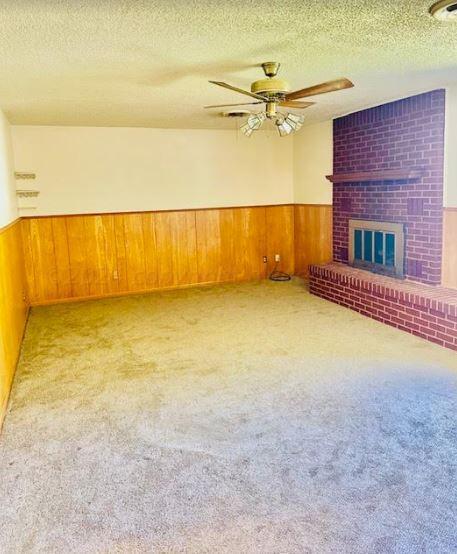 unfurnished living room with light colored carpet, wooden walls, a textured ceiling, ceiling fan, and a fireplace