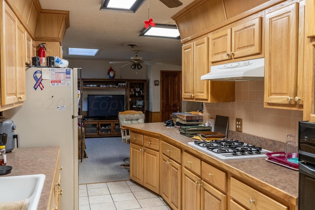 kitchen featuring light tile patterned floors, sink, ceiling fan, a skylight, and white appliances