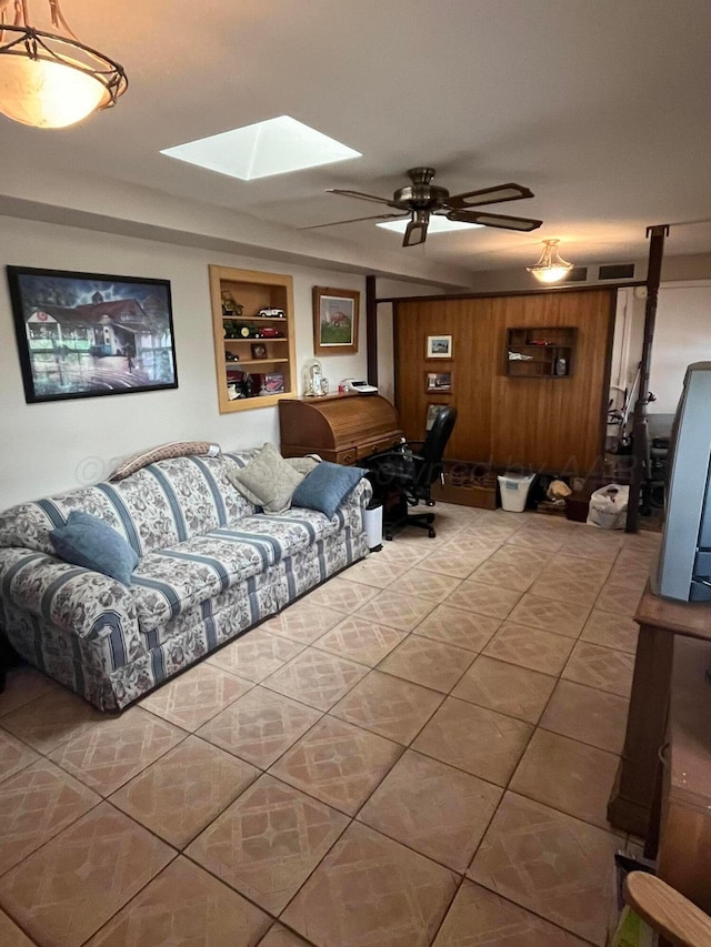 tiled living room with built in features, a skylight, wooden walls, and ceiling fan