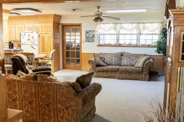 carpeted living room with wood walls, ceiling fan, and a textured ceiling