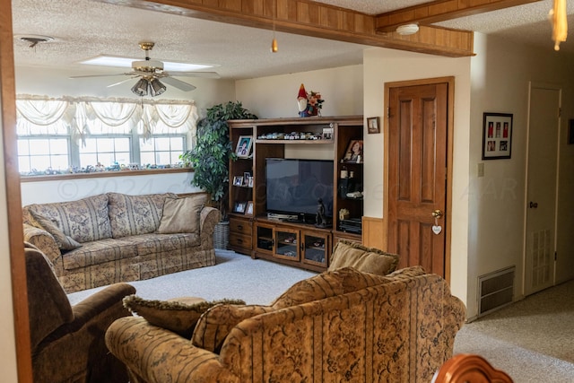 living room with a textured ceiling, carpet, beamed ceiling, and ceiling fan