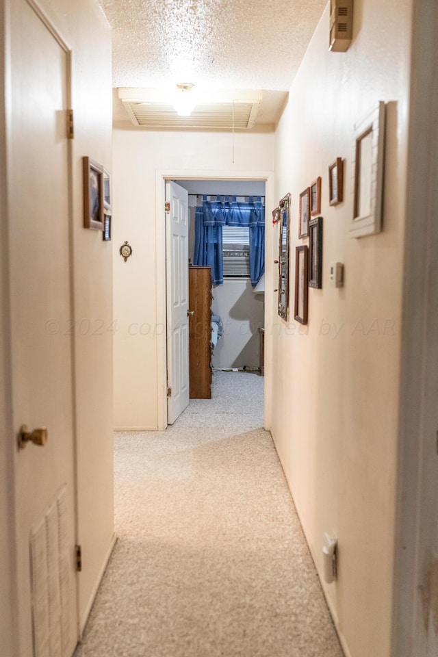 hall with light colored carpet and a textured ceiling