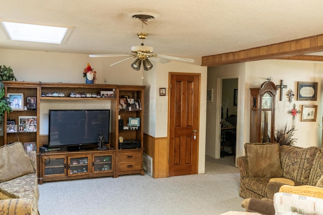 living room featuring wood walls, ceiling fan, a skylight, and light carpet