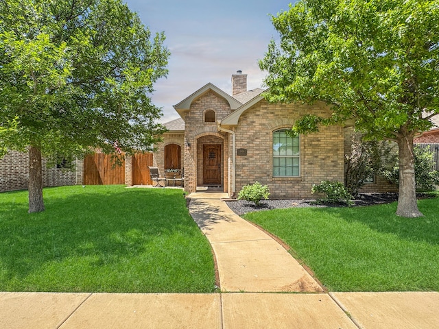 french country inspired facade with a chimney, a front lawn, and brick siding