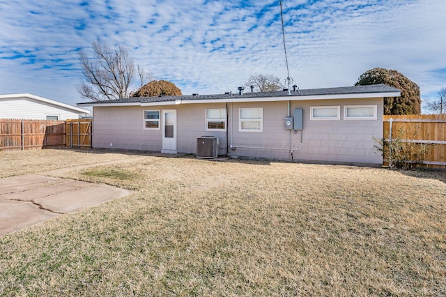 rear view of house with central AC unit and a yard