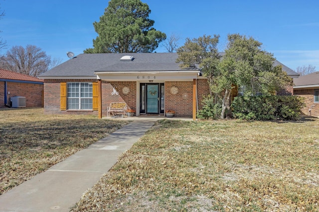 view of front of house with central AC, brick siding, a front yard, and a shingled roof