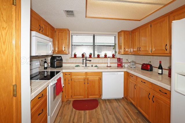 kitchen featuring white appliances, a sink, light wood finished floors, decorative backsplash, and tile counters